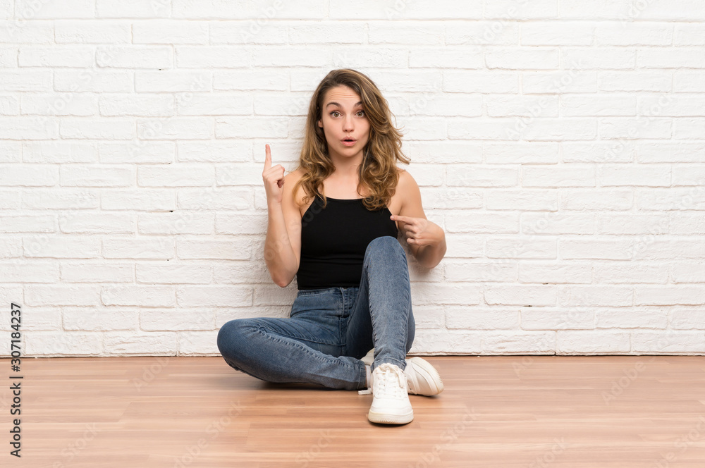 Young blonde woman sitting on the floor with surprise facial expression Young blonde woman sitting on the floor with surprise facial expression