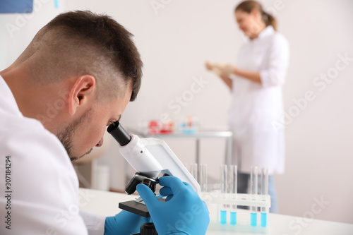 Scientist using microscope at table and colleague in laboratory. Medical research