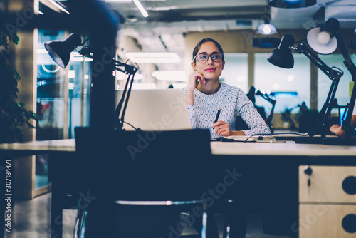Skilled female office worker sitting at desktop with laptop computer creating project planning,young woman in eyewear writing creative ideas for startup using netbook for research at working place