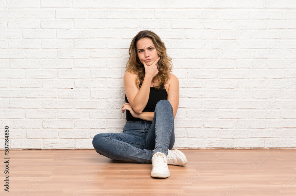 Young blonde woman sitting on the floor thinking an idea Young blonde woman sitting on the floor thinking an idea