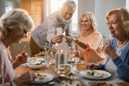 Happy senior couple using mobile phone and taking selfie at dining table.