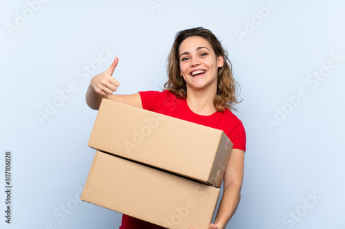 Young blonde woman holding a box to move it to another site with thumb up