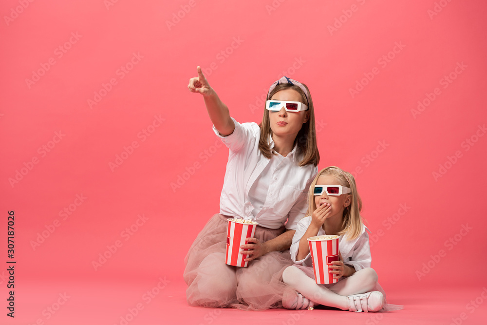 daughter eating popcorn and mother pointing with finger on pink background