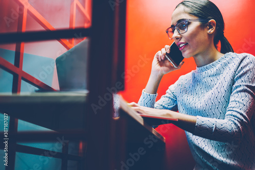 Female manager having mobile phone conversation sitting in noise insulance booth in office getting information,businesswoman talking on smartphone in silence of cabin using laptop for checking data