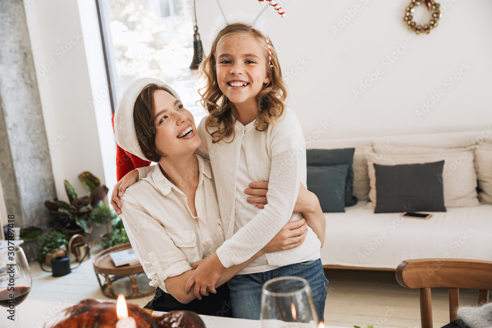 Happy mother hugging her daughter while sitting at the table Happy mother hugging her daughter while sitting at the table