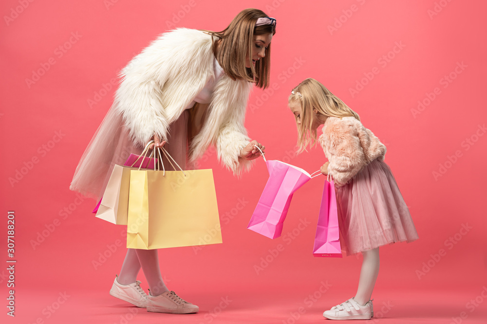 shocked daughter and mother looking at shopping bag on pink background shocked daughter and mother looking at shopping bag on pink background