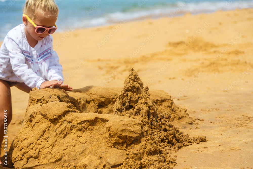 little girl in sunglasses builds sand castle on the ocean shore little girl in sunglasses builds sand castle on the ocean shore