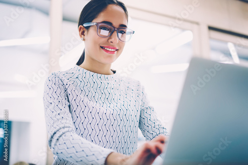 Positive female administrative manager typing feedback for clients comments on web pege working in clinic,smiling woman in spectacles making online research for report keyboarding on netbook photo