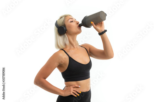 blonde girl in a sports uniform drinks water listens to music on a white background
