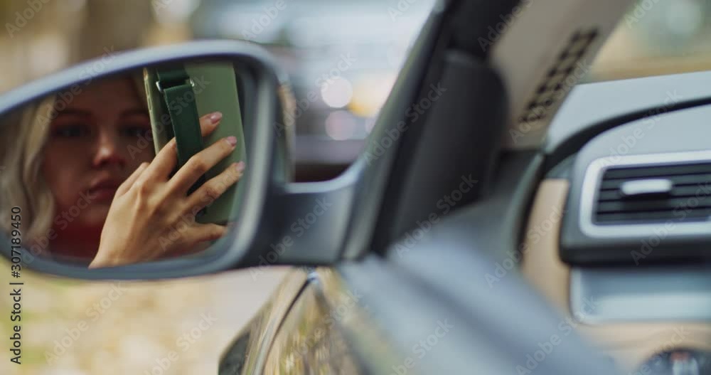 Stylish pensive woman using smartphone device sitting on driver seat of modern luxury car. Mirror reflection view. Blonde girl surfing online looking for center area. Navigation app. Map application. Stylish pensive woman using smartphone device sitting on driver seat of modern luxury car. Mirror reflection view. Blonde girl surfing online looking for center area. Navigation app. Map application.