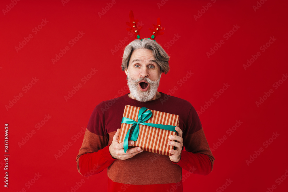 Portrait of gray-haired old man in sweater holding Christmas gift box
