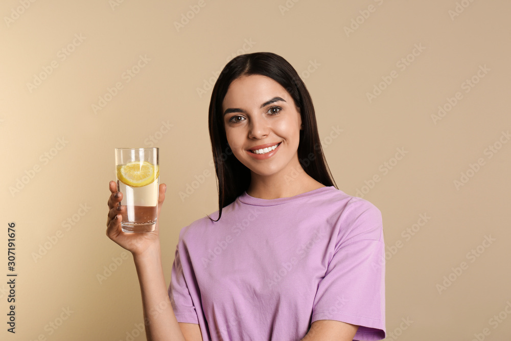 Beautiful young woman with tasty lemon water on beige background Beautiful young woman with tasty lemon water on beige background