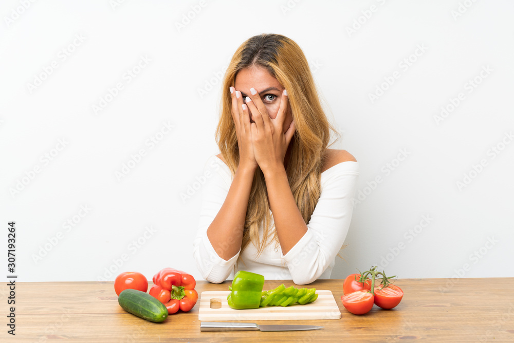 Young blonde woman with vegetables in a table covering eyes and looking through fingers Young blonde woman with vegetables in a table covering eyes and looking through fingers