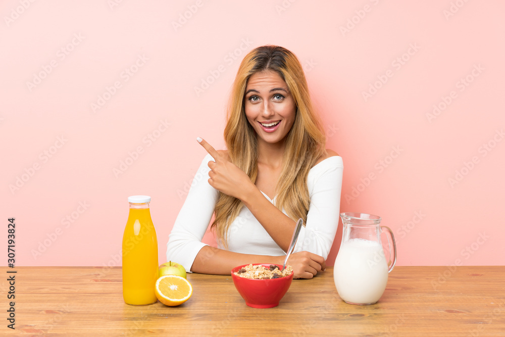 Young blonde woman having breakfast milk pointing finger to the side Young blonde woman having breakfast milk pointing finger to the side