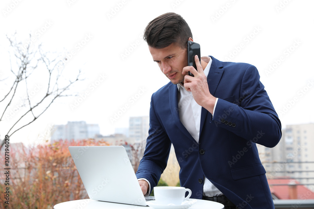 Businessman with laptop talking on phone in outdoor cafe. Corporate blog Businessman with laptop talking on phone in outdoor cafe. Corporate blog