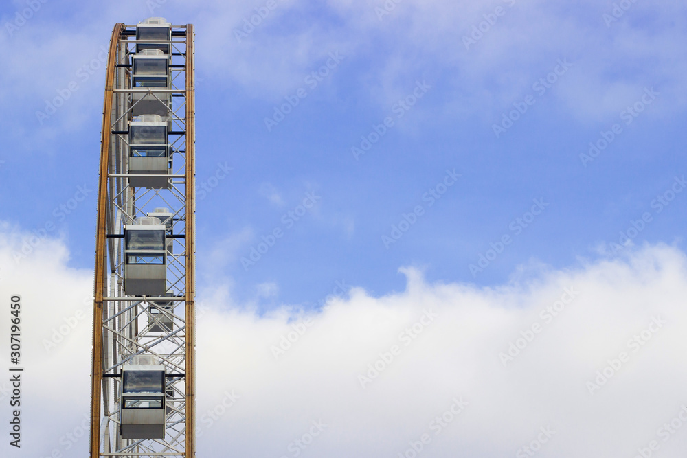 view from the side of a ferris wheel made of glass and metal against a blue sky. view from the side of a ferris wheel made of glass and metal against a blue sky.