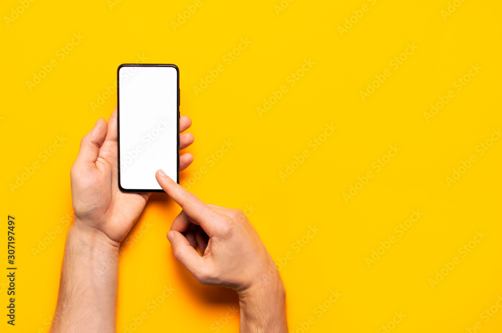 Male hands hold a modern black smartphone with white blank screen on yellow background. Modern technology, phone, gadget in hands, touch screen, template for your design. Mockup