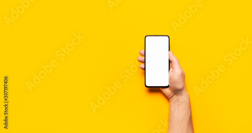 Male hands hold a modern black smartphone with white blank screen on yellow background. Modern technology, phone, gadget in hands, touch screen, template for your design. Mockup