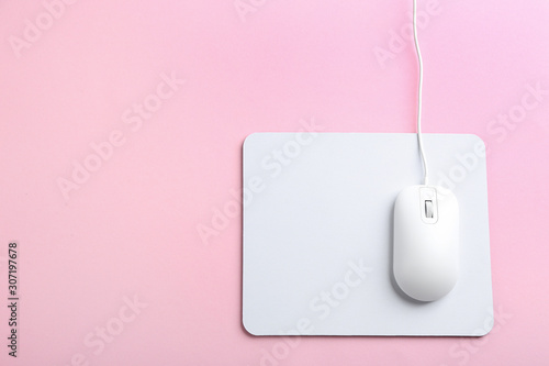 Modern optical wired mouse and white pad on pink background, top view. Space for text