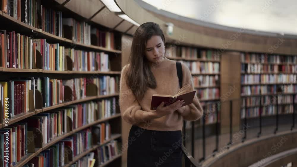 Girl student holding in hands studies with enthusiasm reads a book or textbook in the university library. Girl student holding in hands studies with enthusiasm reads a book or textbook in the university library.