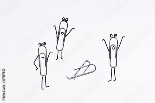 Paper clips are lying on a white surface - one of the paper clips is broken, the remaining paper clips crowded around