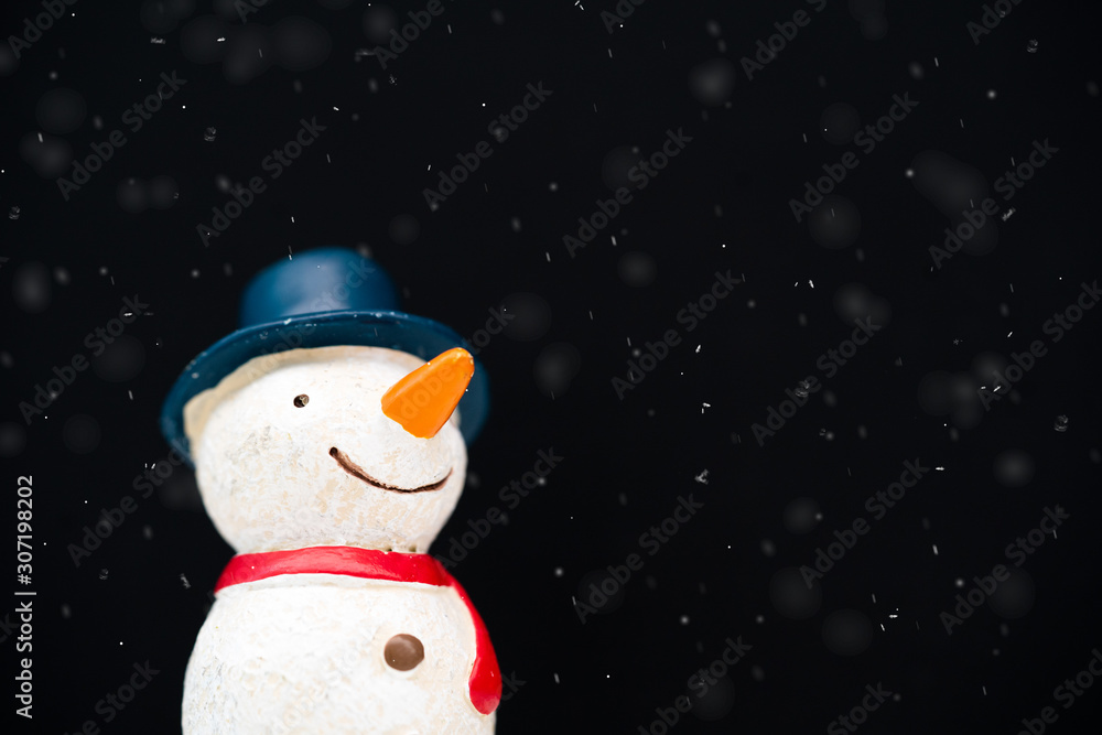 Fototapeta premium Happy smiley snowman wear blue hat and carrot nose standing with snowflakes in winter christmas season.Black background.Christmas scenes.