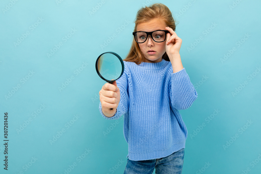 curious european girl in glasses looks through a magnifying glass on a light blue background curious european girl in glasses looks through a magnifying glass on a light blue background
