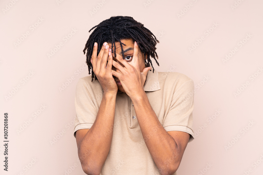 Young African American man over isolated background covering eyes and looking through fingers Young African American man over isolated background covering eyes and looking through fingers