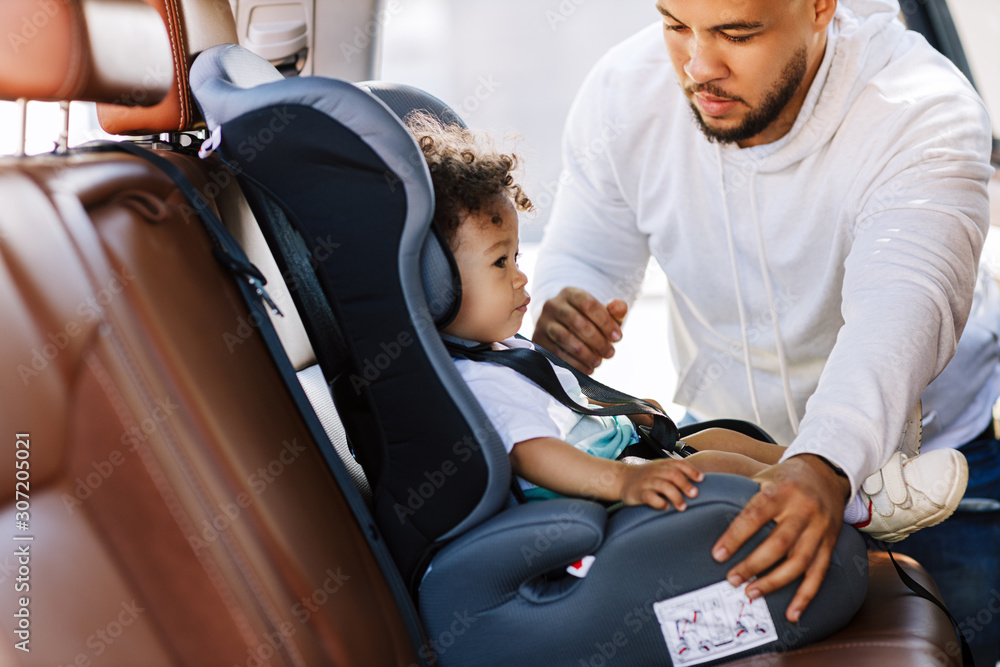 Obraz premium Young parent adjusting safety seat for his little son 