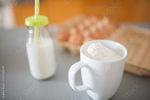 Mug with flour and bottle of milk on kitchen table