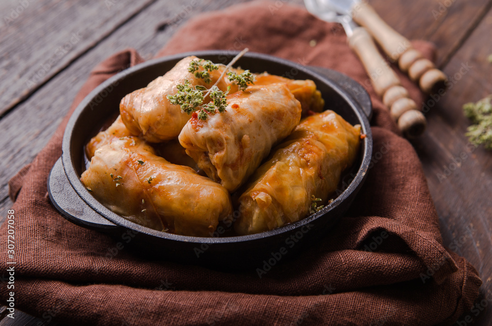 Meat in cabbage rolls in a black pan with sauce on wooden background. Asian cuisine top view Meat in cabbage rolls in a black pan with sauce on wooden background. Asian cuisine top view