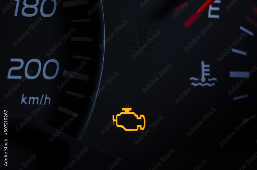 Yellow lit engine error sign on car dashboard close up