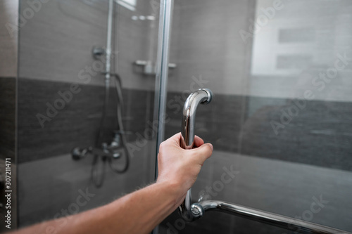 Male hand opens the shower door in a modern bathroom.