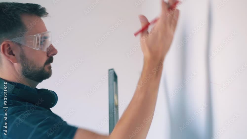 CU: upset young man in blue shirt and protective glasses checks wall level with modern instrument at room renewal closeup CU: upset young man in blue shirt and protective glasses checks wall level with modern instrument at room renewal closeup