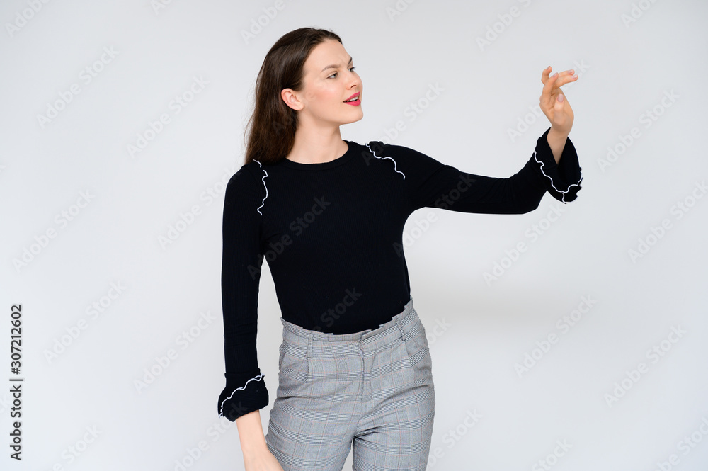 Concept adult girl on a white background. A photo of a pretty brunette girl in gray trousers and a black sweater smiles and shows different emotions in different poses right in front of the camera. Concept adult girl on a white background. A photo of a pretty brunette girl in gray trousers and a black sweater smiles and shows different emotions in different poses right in front of the camera.