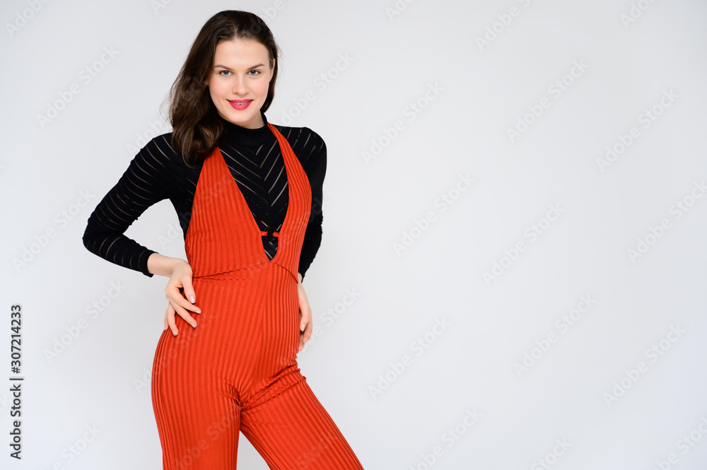 Concept adult girl on a white background. A photo of a pretty brunette girl in red trousers and a black sweater smiles and shows different emotions in different poses right in front of the camera. Concept adult girl on a white background. A photo of a pretty brunette girl in red trousers and a black sweater smiles and shows different emotions in different poses right in front of the camera.