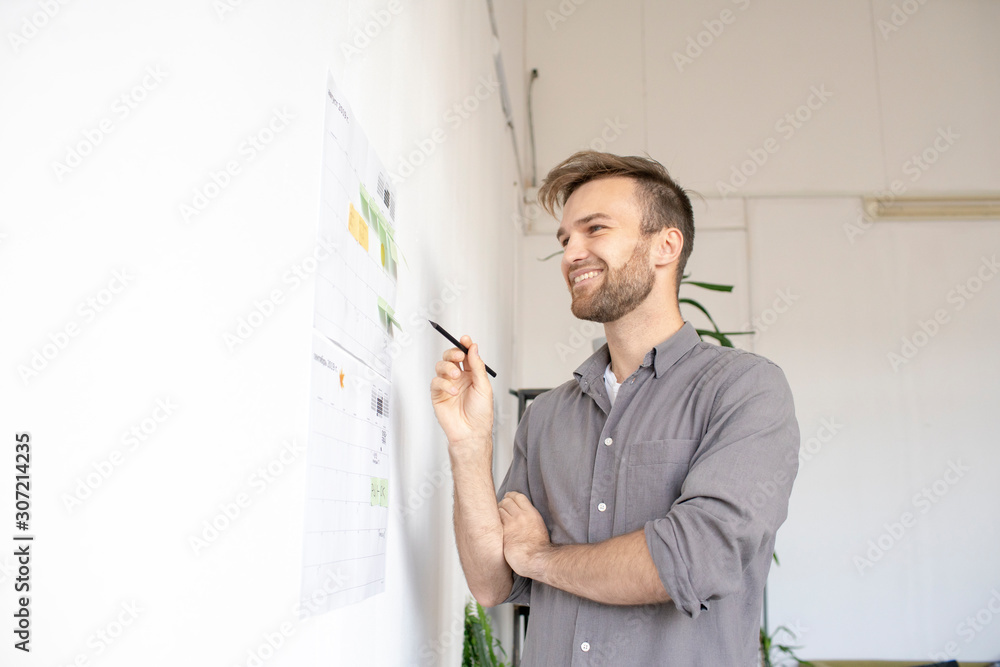 Smiling man working on paper at the wall in office Smiling man working on paper at the wall in office