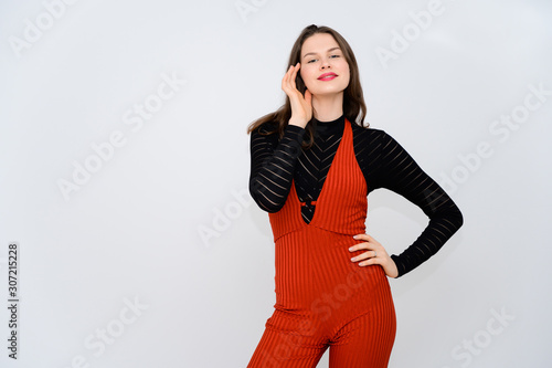 Concept adult girl on a white background. A photo of a pretty brunette girl in red trousers and a black sweater smiles and shows different emotions in different poses right in front of the camera. © Вячеслав Чичаев