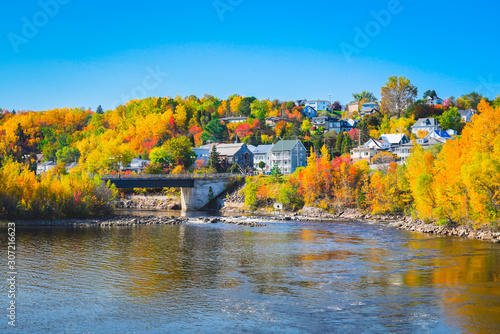 Autumn Landscape View of Village on Shore of Lake with Colorful Trees, River and Bridge against Blue Sky Reflected in Water photo