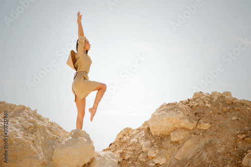 Slim girl in Vietnamese style khaki dress stands on sand dunes, yoga