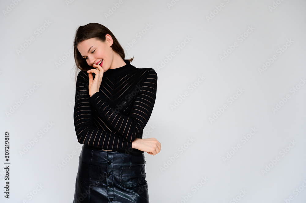 Concept adult girl on a white background. A photo of a pretty brunette girl in a black skirt and black sweater smiles and shows different emotions in different poses right in front of the camera. Concept adult girl on a white background. A photo of a pretty brunette girl in a black skirt and black sweater smiles and shows different emotions in different poses right in front of the camera.