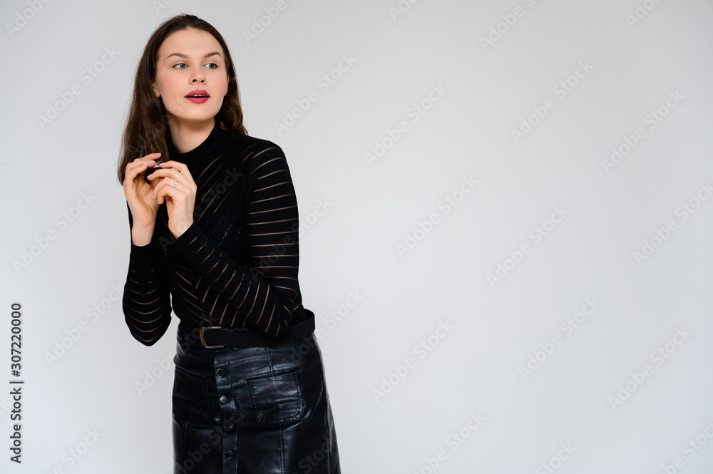 Concept adult girl on a white background. A photo of a pretty brunette girl in a black skirt and black sweater smiles and shows different emotions in different poses right in front of the camera. Concept adult girl on a white background. A photo of a pretty brunette girl in a black skirt and black sweater smiles and shows different emotions in different poses right in front of the camera.