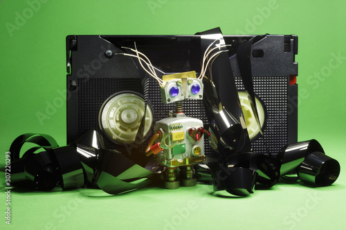 Funny robot-cyborg with VHS video tapes and film on a green background. 