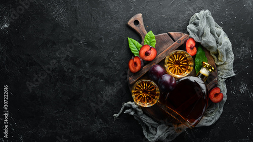 Fotografie Slivovica - plum vodka, plum brandy in a bottle on a black stone table