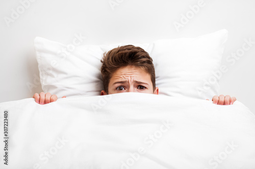 Scared peeking child boy lying bed covering face with blanket © ia_64