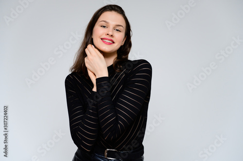 Concept adult girl on a white background. Large photo of a pretty brunette girl in a black sweater smiling and showing different emotions in different poses right in front of the camera.