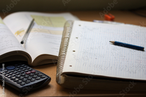 A notebook with math exercises written in pencil next to a calculator