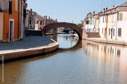 Comacchio , Italy, beautiful town with its narrow streets, canals and bridges. Houses reflected in the water under a clean blue sky.