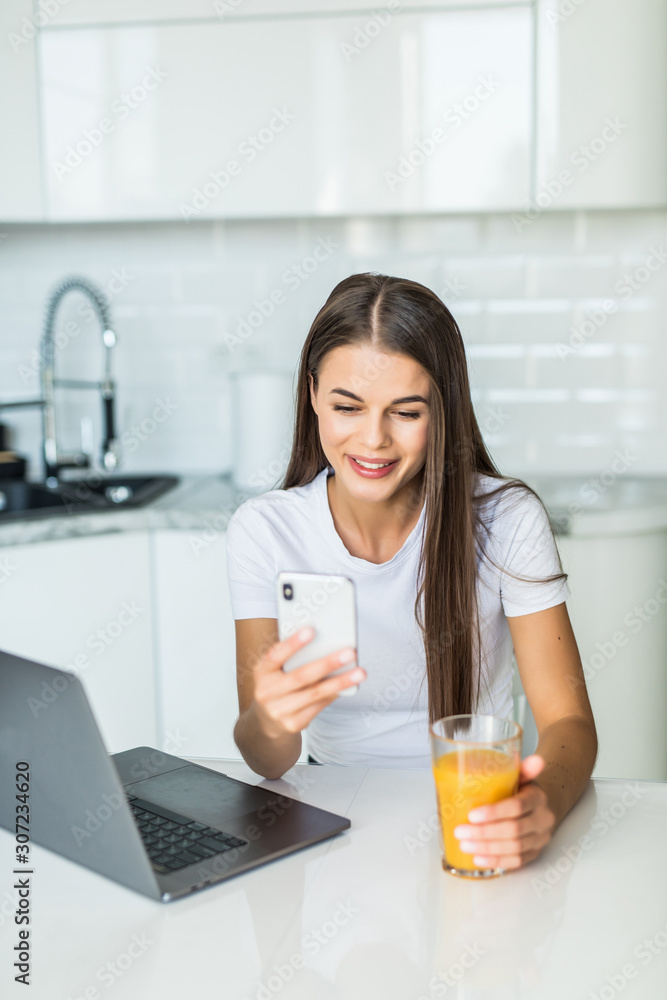 Beautiful young woman working on laptop use phone in the kitchen Beautiful young woman working on laptop use phone in the kitchen