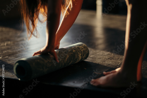 A girl rolls a rug with her hands and stands on toes on the floor for yoga in a fitness studio or at home in sunny weather
